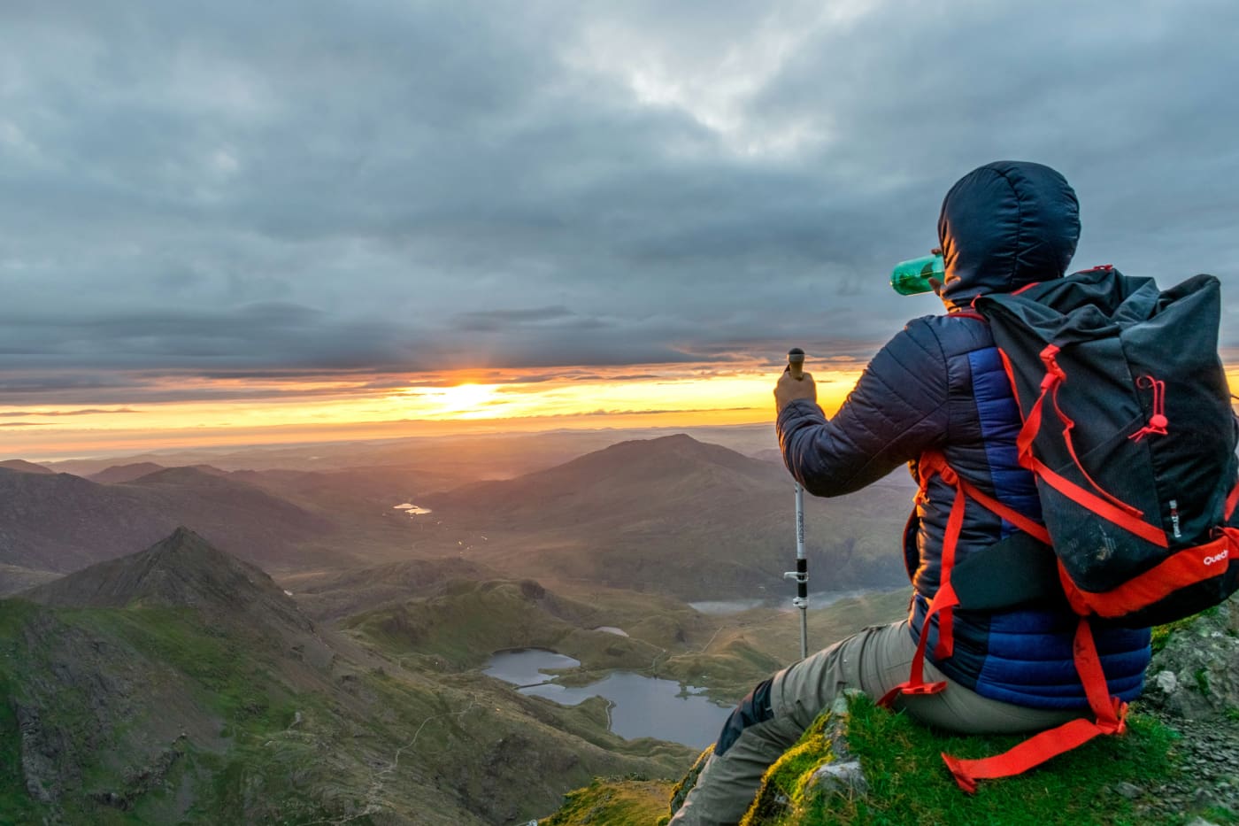 A man standing on top of a mountain looking at the sunset.